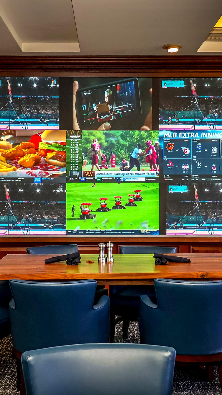 Large multi-screen video wall displaying various broadcasts in a dining room