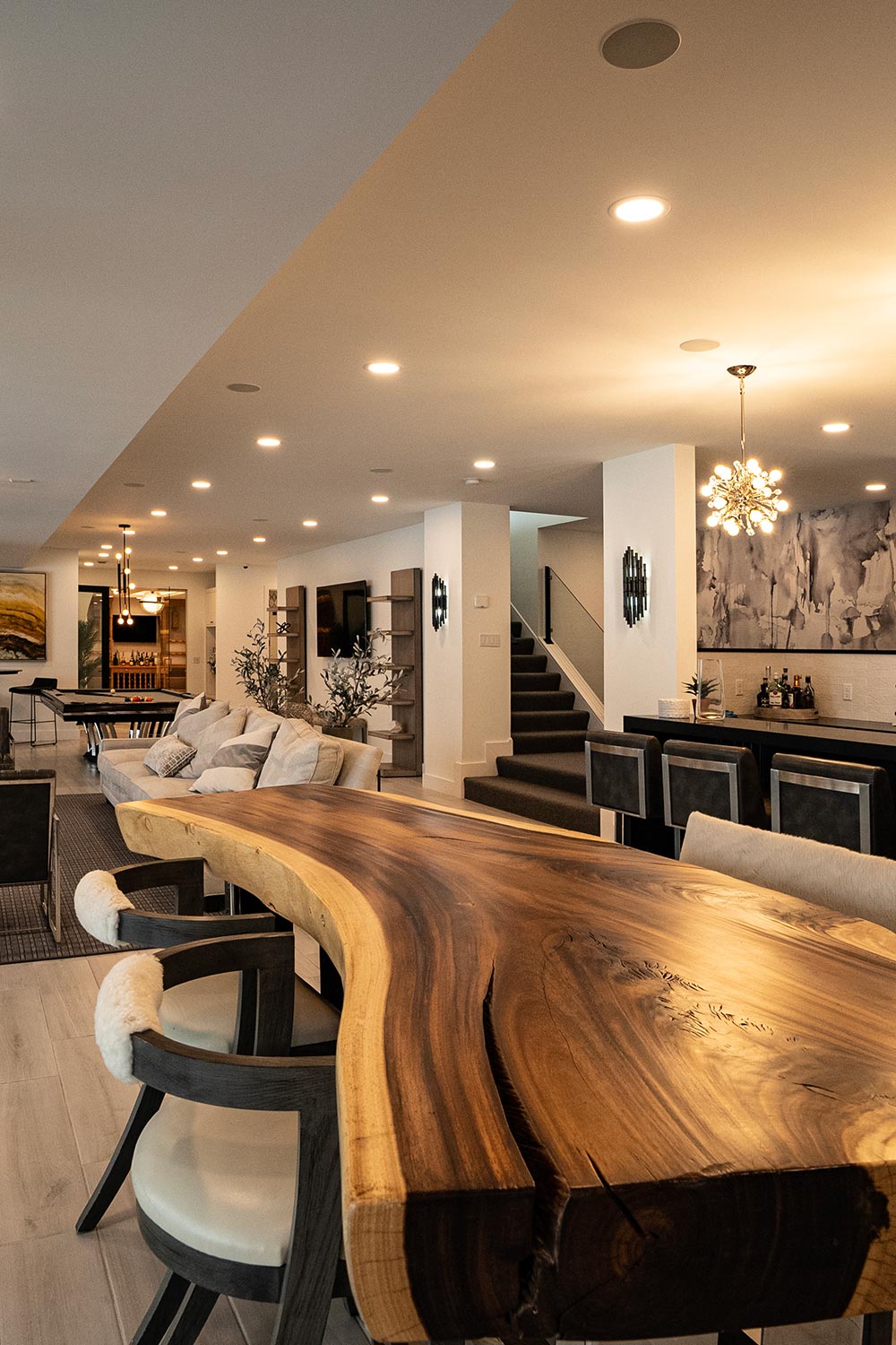 Modern open-concept living space with a live-edge wooden table and recessed ceiling speakers