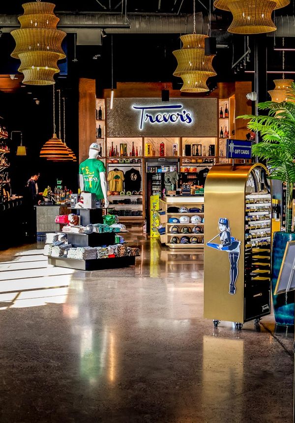 View through a tiled archway into the main retail space featuring a "Trevor's" neon sign and merchandise displays.