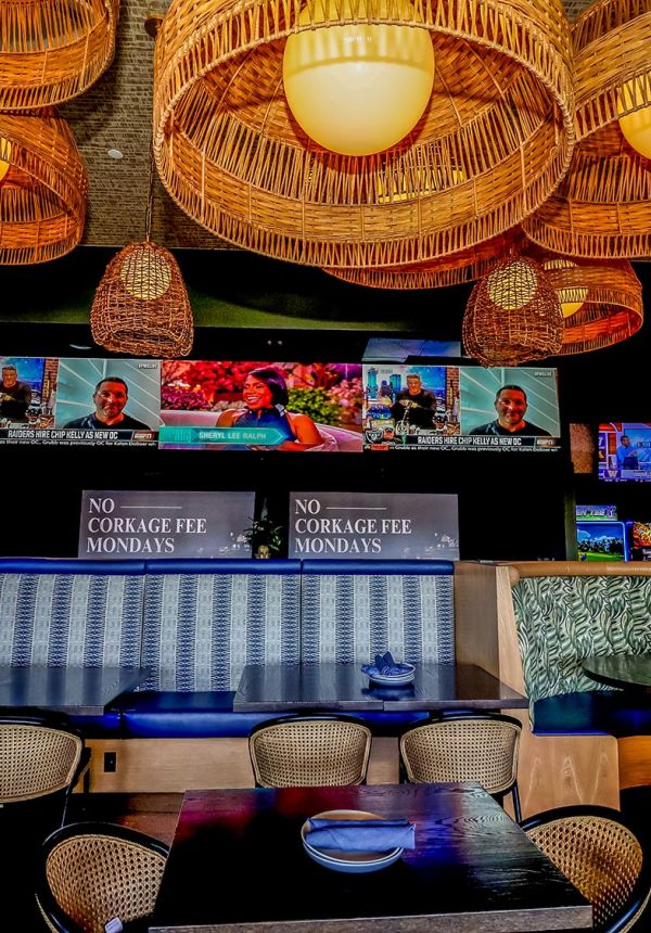 Interior restaurant seating with blue booths, woven light fixtures, and multiple large TVs showing sports news.